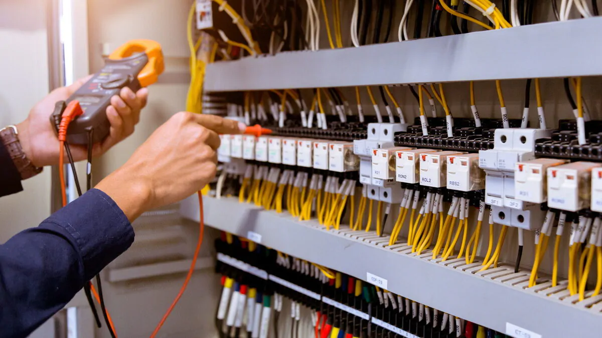 Electrician measurements with multimeter testing current electric in control panel.